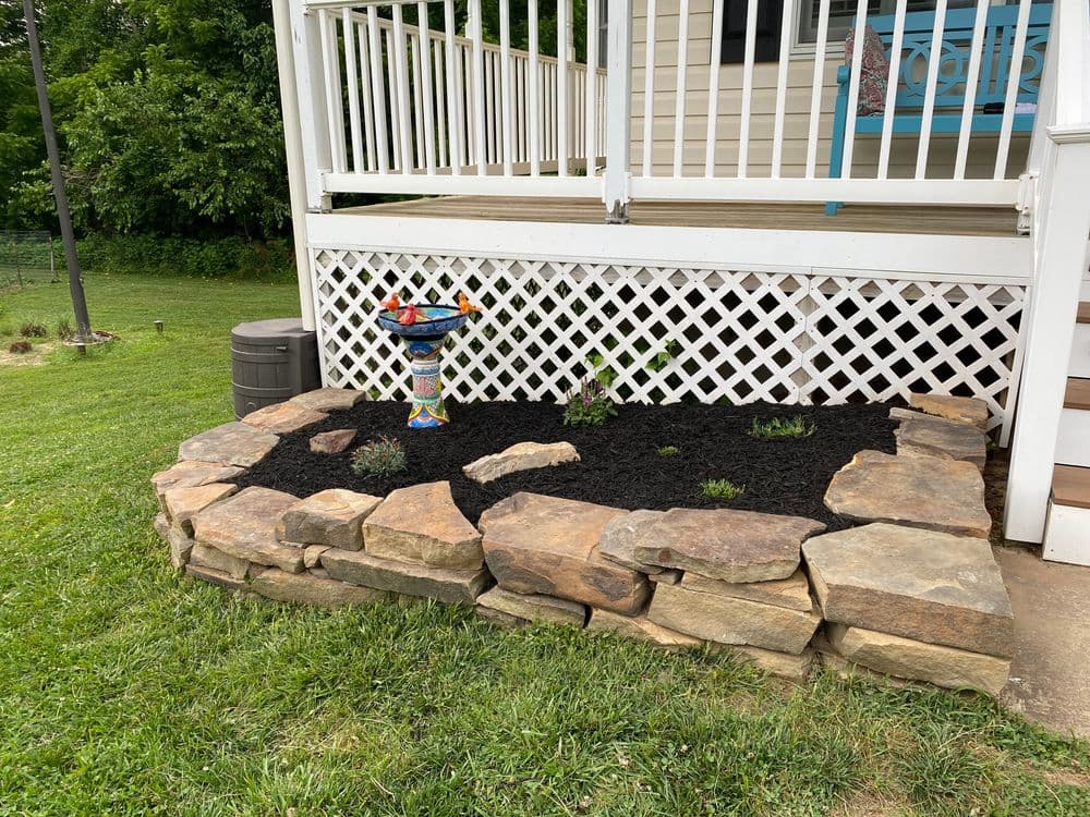 Colorful birdbath in a landscaped rock garden with black mulch near a house.