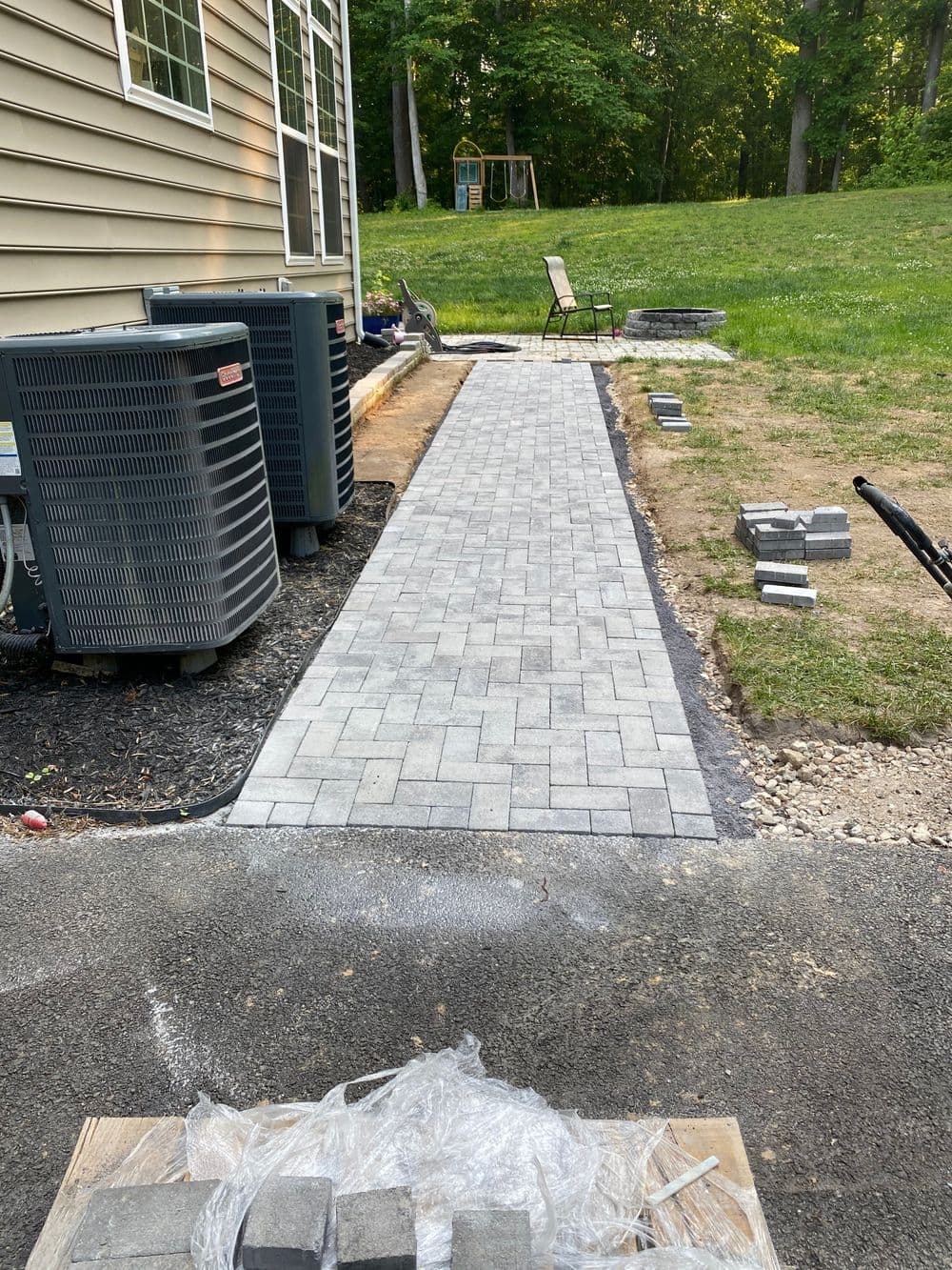 Paver stone walkway alongside a house, leading to a grassy area.