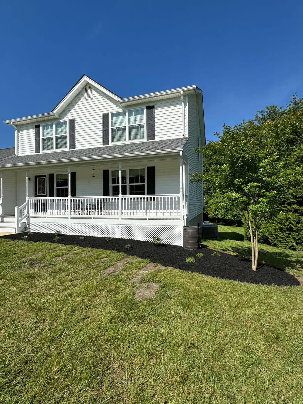 Two-story white house with a porch, green lawn, and landscaping in clear blue sky.
