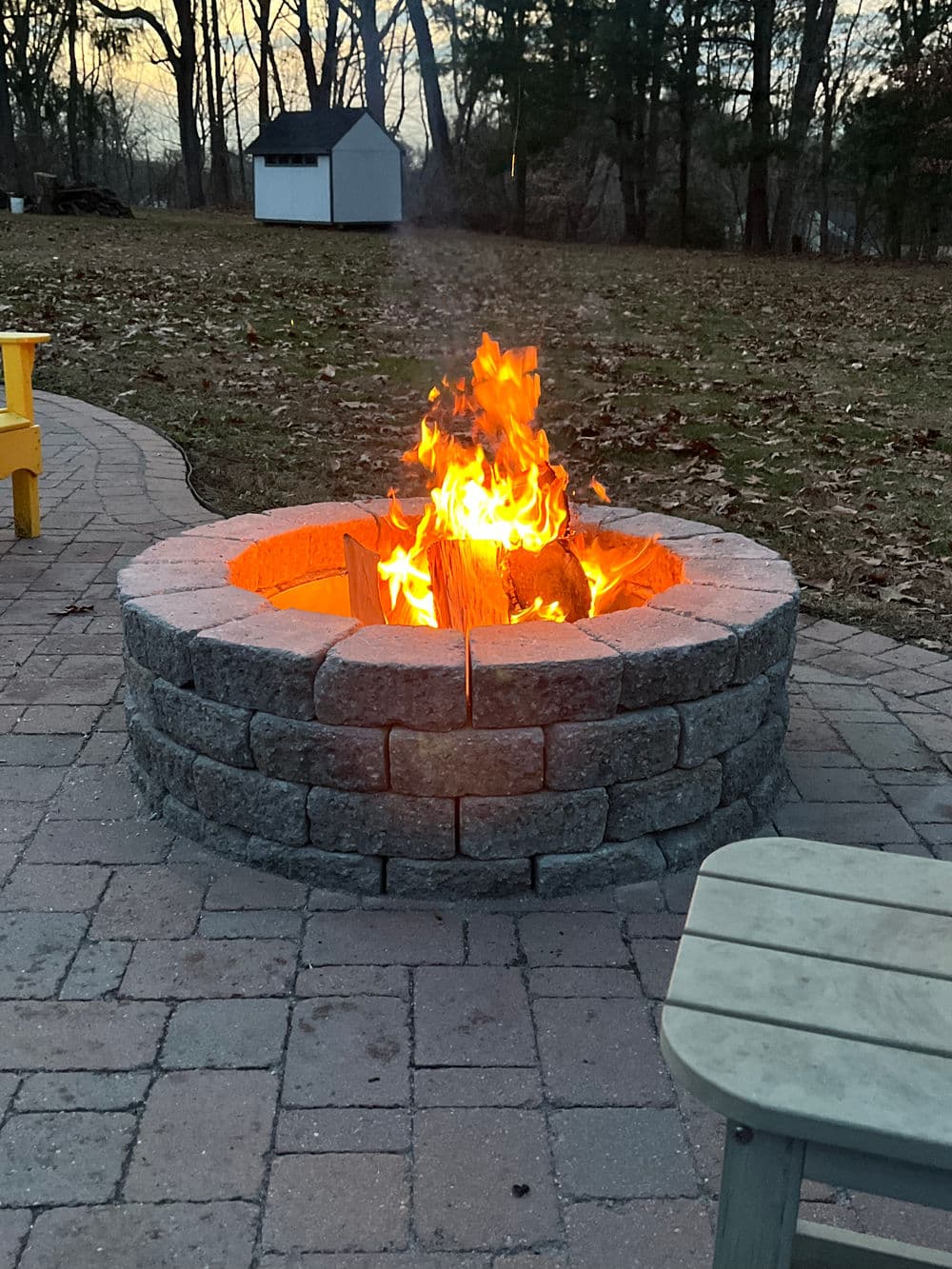 Cozy outdoor fire pit with flames and stone seating in a serene backyard setting.