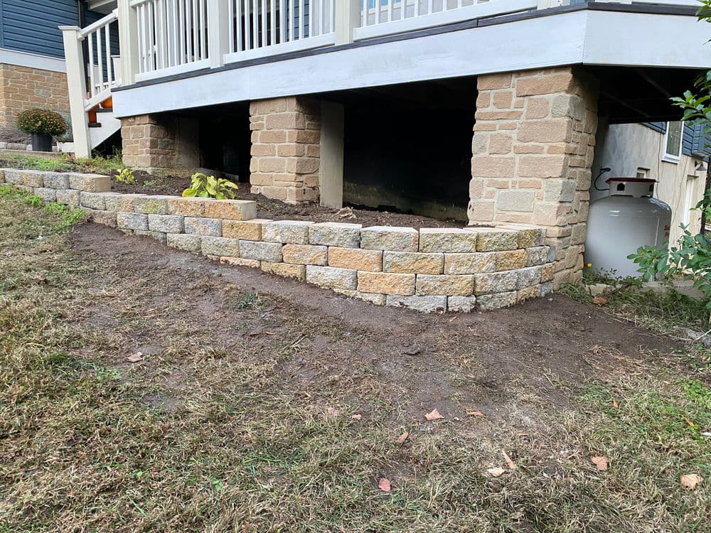 Retaining wall made of stone blocks supports landscaping beneath a wooden deck.
