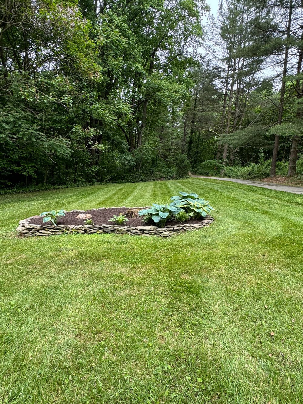 Lush garden with stone border, surrounded by manicured grass and trees in the background.